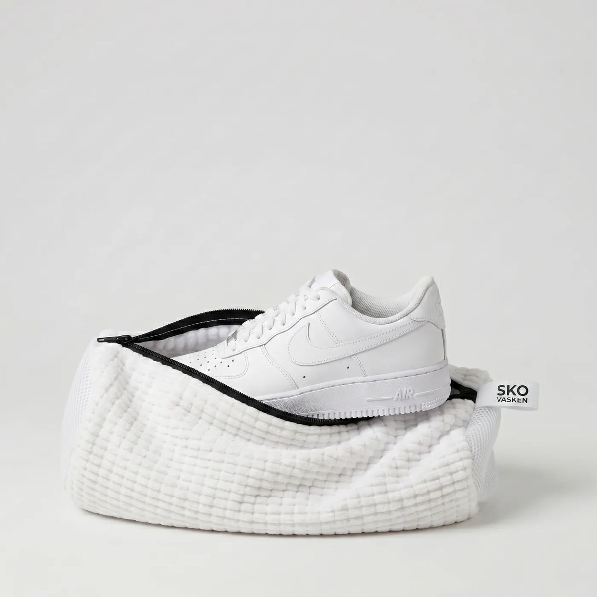 A white Skovasken microfibre wash bag holding a white trainer