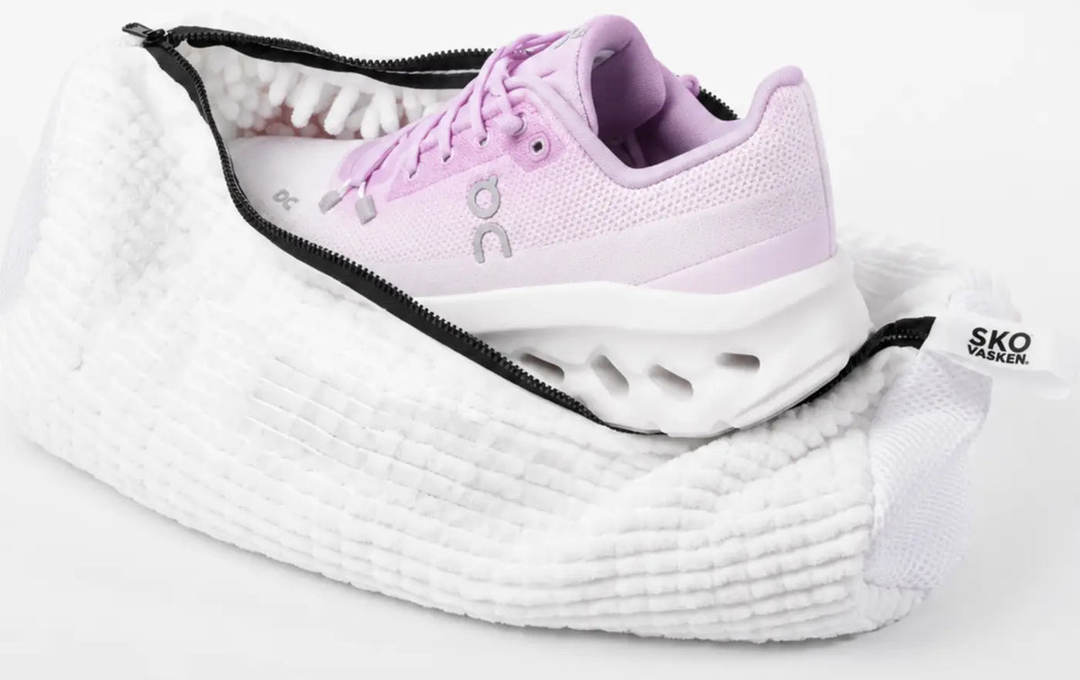 A white Skovasken shoe wash bag, unzipped, holding a lilac running trainer