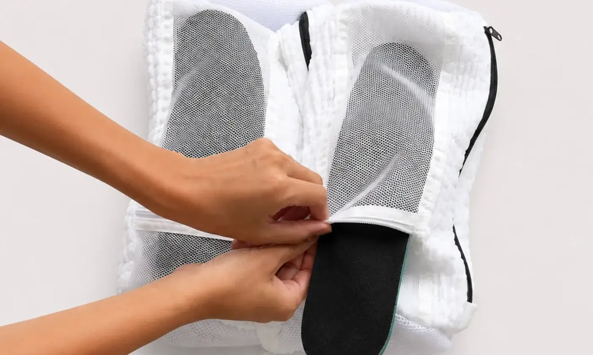 An insole being lifted out of a trainer inside a white Skovasken wash bag